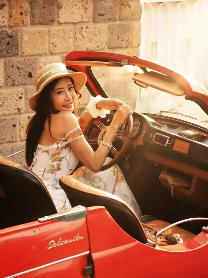 Woman in a straw hat at the wheel of a red vintage convertible during a photo tour